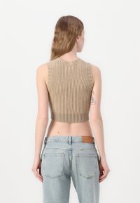 Top court en tricot côtelé beige avec un décolleté rond et sans manches, associé à un jean taille haute bleu clair.