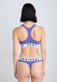 Lilla idretts-bh med racerback-design og en hvit kant med "DKNY" i svart skrift. Matchende lilla bikini-bunn.