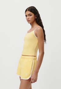 Gul ribbet tank top med hvit kant, sammen med matchende gule shorts med hvite detaljer og logo. Glatt tekstur.