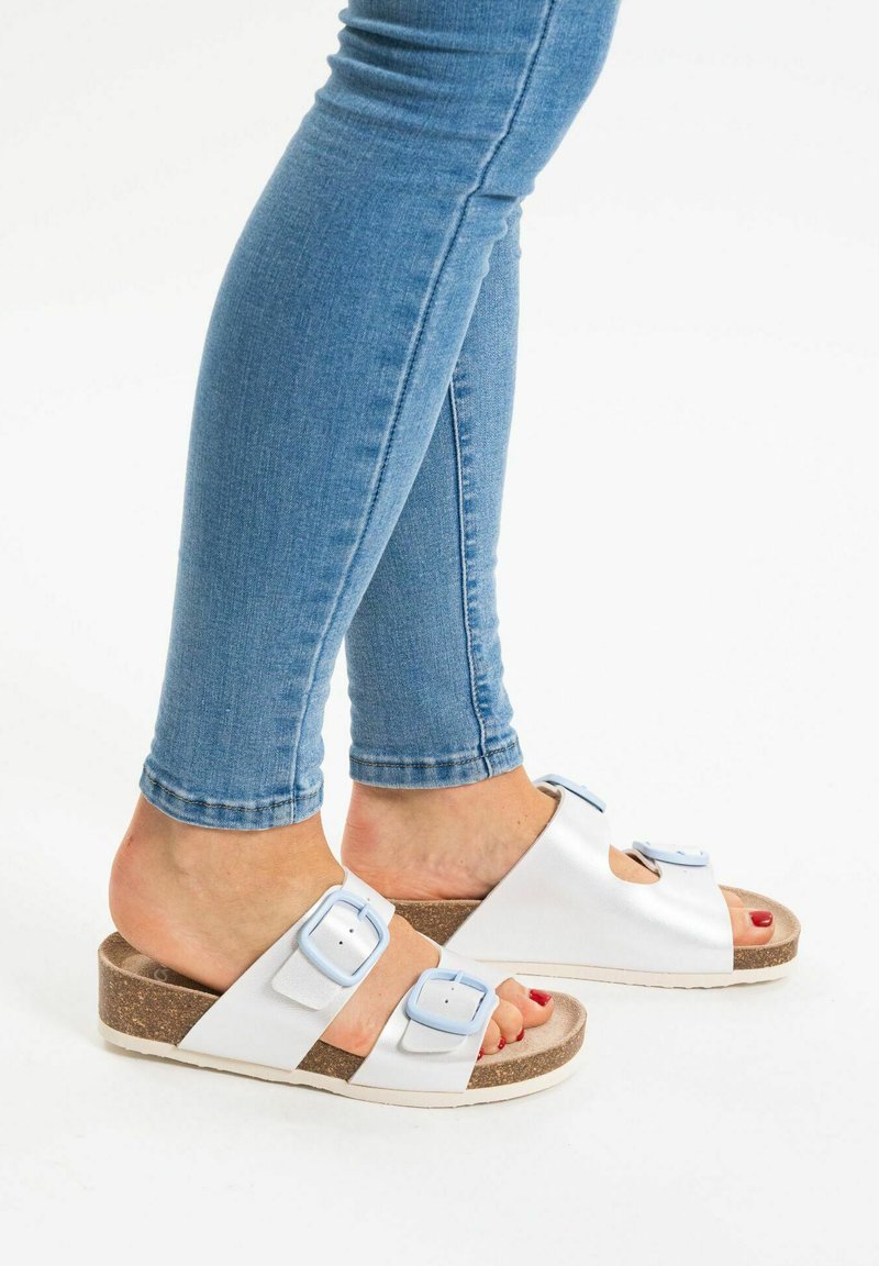 Witte sandalen met twee blauwe gespaccenten, kurken voetbed en open teen ontwerp. Draag met blauwe skinny jeans. Platter zool.