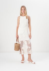 Bela cvetna obleka s prilegajočim korzetom in prosojnim spodnjim delom krila. Kombinirana z pleteno torbico v obliki vedra in svetlimi natikači z zlato obrobo.