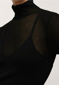 Haut col roulé noir avec une texture transparente et côtelée, doté d'un décolleté en V. Le matériau a une finition lisse, mettant en valeur les détails superposés.