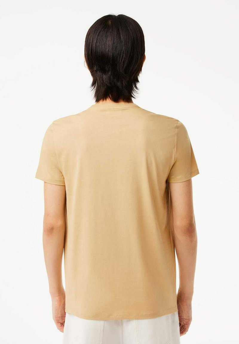 Beżowy t-shirt z krótkim rękawem, wykonany z miękkiej bawełny, z klasycznym okrągłym dekoltem i luźnym krojem, o gładkiej i jednolitej fakturze.