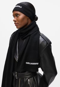 Musta neulottu huivi, jossa on matching-panta, jossa on valkoinen "KARL LAGERFELD" -logo, käytetään nahkatakin kanssa, joka korostaa hopeisia yksityiskohtia.