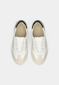 Sneaker bianche in pelle con accenti in suede beige, un cappuccio del tallone nero e lacci bianchi. Presentano una finitura liscia e texture contrastanti.