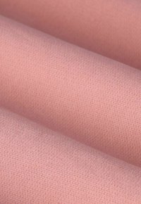 Tissu en teinte rose douce, présentant une texture lisse avec un léger motif de tissage. Des rouleaux de tissu exposés de près.