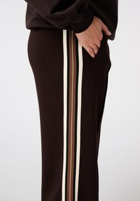 Pantalons de jogging marron avec des rayures latérales en crème, noir et marron, dotés d'une poche et d'un tissu souple et extensible.