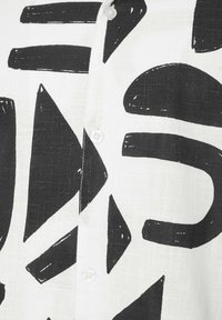 Tissu blanc avec des formes géométriques noires audacieuses, y compris des triangles et des rectangles, avec des boutons blancs visibles le long d'une couture centrale.