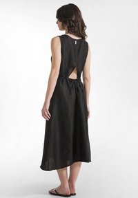 Vestido negro sin mangas con abertura en la espalda y cintura con cordón. Hecho de tela ligera y texturizada, con caída hasta la mitad de la pantorrilla.