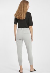 Pantalons de yoga gris avec un design fuselé, taille élastique, détail de poche arrière, associés à un haut noir à manches courtes et des sandales noires.