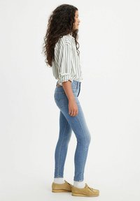 Jeans skinny de color azul claro combinados con una camisa blanca a rayas y zapatos slip-on beige. El atuendo presenta un diseño ajustado y mangas arremangadas.