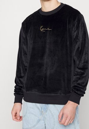 Felpa in velluto nero con una texture liscia, caratterizzata da un logo ricamato in oro sul petto e polsini e orlo a coste a contrasto.