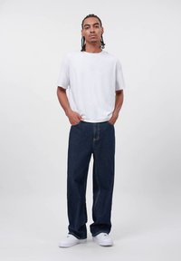 Vit t-shirt med korta ärmar, blåa löst sittande jeans och vita sneakers. Enkel design, avslappnad passform och enfärgade utan mönster.