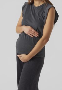 Tmavě šedé tričko s krátkým rukávem v kombinaci s odpovídajícími kalhotami, které jsou na břiše těsné. Materiál vypadá měkký a elastický.