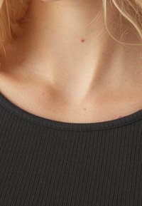 Svart ribbat tyg med en bred, rundad halsringning; slät textur; synlig hudton under kragen. Inga mönster eller detaljer förekommer.