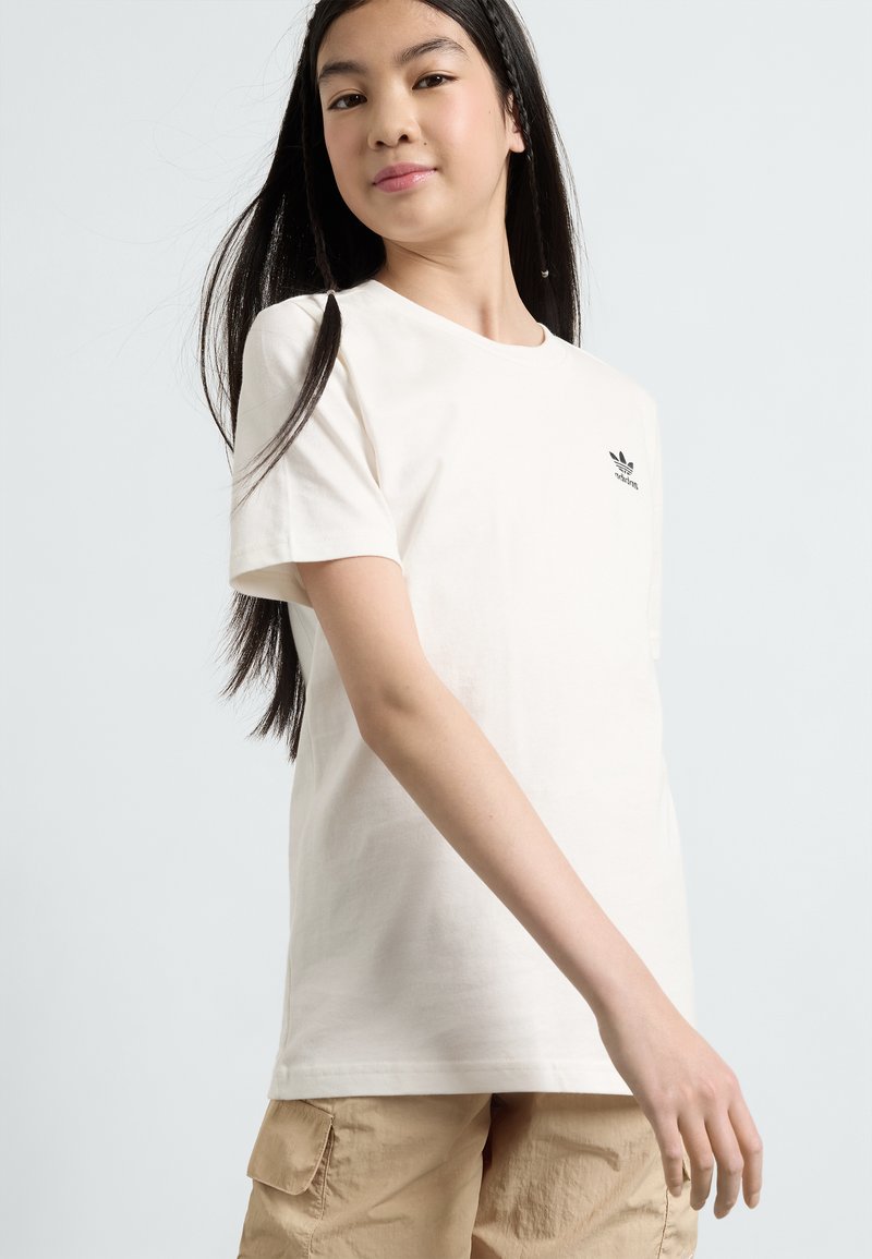T-shirt en coton blanc avec un petit logo noir sur la poitrine. Manches courtes, encolure ronde et coupe décontractée. Stylis�é avec un pantalon cargo beige.