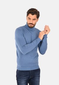 Maglione a collo alto azzurro chiaro realizzato in morbido tessuto a maglia, con polsini e orlo a coste. Indossato con jeans in denim scuro.