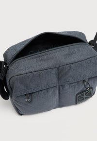 Γκρι τσαντάκι ώμου από νάιλον με γεωμετρικό μοτίβο, κορυφαίο φερμουάρ, δύο μπροστινές τσέπες και υφασμένη ετικέτα με το λογότυπο.