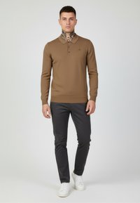 Brown long-sleeve polo with a textured design and three-button placket, paired with slim-fit black pants and white sneakers.
