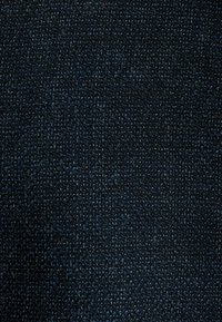 Tyg i mörkblå nyanser med en texturerad väv, som visar ett tätt stickat mönster och en lätt lyster över hela ytan.