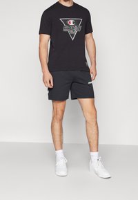 Mustan lyhythihaisen t-paidan etuosassa on kolmion muotoinen logo, jossa lukee "CHAMPION". Yhdistetty mustiin urheilushortseihin ja valkoisiin lenkkitossuihin.