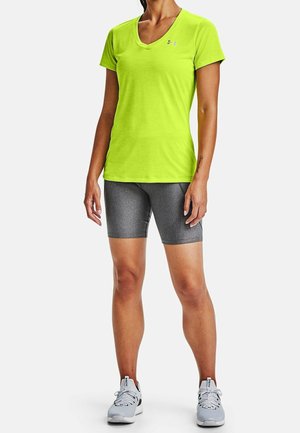 Limegrön kortärmad träningströja med V-ringning, i kombination med grå åtsittande shorts. Lättvikts, slätt tyg. Inga mönster eller utsmyckningar.