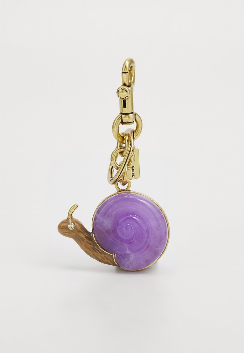 Chaveiro em forma de caracol com uma concha de resina roxa, detalhes em metal dourado e um pequeno strass na cabeça do caracol.