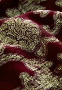 Tejido rojo oscuro con intrincados patrones florales y de scroll en oro, mostrando textura y pliegues.