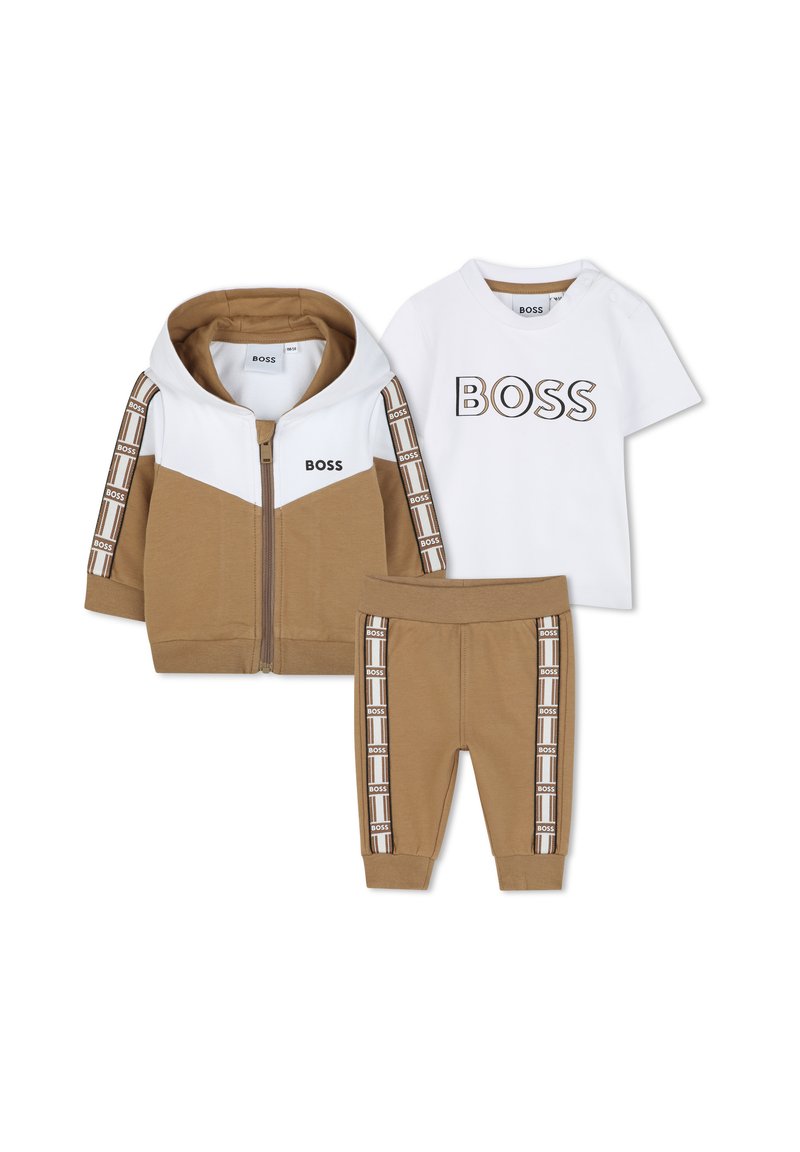 Conjunto de tres piezas en beige y blanco que incluye una sudadera con cremallera, una camiseta blanca con el logo "BOSS" y pantalones a juego con acentos del logo.