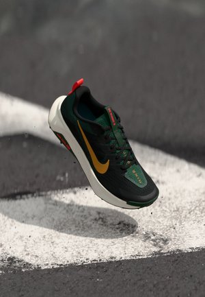 Black and green athletic shoe with a yellow swoosh, mesh upper, red accents, and a white sole, suspended above a concrete surface.