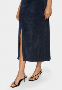 Rochie midi din catifea cord cu dungi verticale și fanta laterală. Asortată cu sandale cu toc înalt, negre, cu curea, evidențiind un design minimalist.