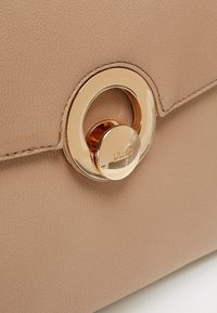 Gros plan d'un sac à main en cuir beige avec une fermeture twist-lock ronde en or gravée du nom de la marque.