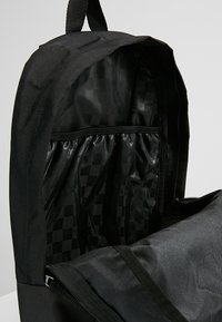 Zaino nero con chiusura a zip, dotato di un interno a motivo a scacchi e un ampio scomparto principale. Tessuto resistente e spallacci robusti.