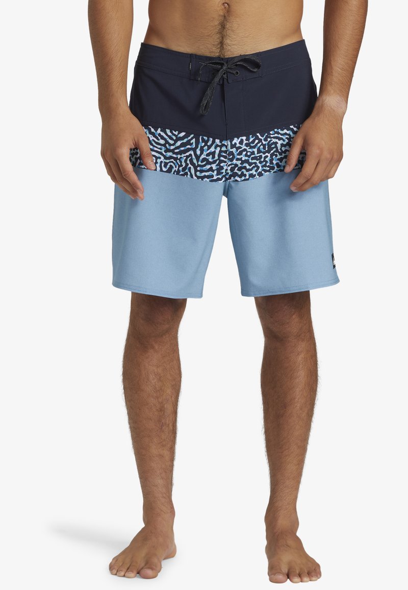 Shorts de bain bleus avec une ceinture noire, un motif corail coloré et une texture lisse. Couture apparente avec des détails de poches latérales.