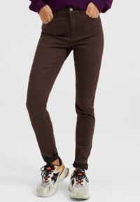 Ruske farkkuhousut, joissa on kapea malli, nappikiinnitys ja kierretut lahkeet, yhdistettyinä monivärisiin urheilukenkiin.