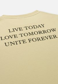 Korte mouwen, lichtgele katoenen t-shirt met opvallende zwarte tekst: "LEEF VANDAAG DOE VANDAAG LIEFDE VOOR ALTIJD" op de achterkant.