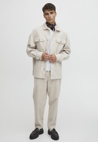 Cream corduroy shirt jacket with two front pockets, paired with matching ribbed pants. Black chunky loafers accentuate the outfit.