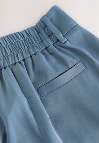 Pantaloni di tessuto leggero blu con vita elasticizzata. Presentano una texture liscia e una tasca posteriore rettangolare con contorno cucito.