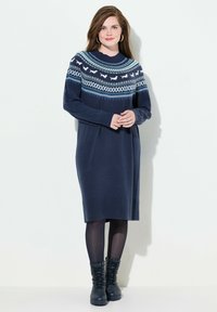 Abito maglione blu navy con maniche lunghe, caratterizzato da una yoke a fantasia blu e bianca. Polsini e orlo a costine, abbinato a stivali neri con lacci.