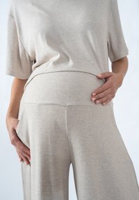 Helles beiges, geripptes Umstandsoutfit mit einem locker sitzenden Oberteil mit kurzen Ärmeln und hoch taillierten, weit geschnittenen Hosen. Weiche Textur.