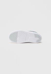 Λευκό πέλμα αθλητικού παπουτσιού με υφή στην επιφάνεια για καλύτερο κράτημα, που περιλαμβάνει στρογγυλεμένο τακούνι, ελαφρώς διάφανο τμήμα και έντονη λεπτομέρεια με το λογότυπο.