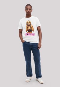 Weißes Baumwoll-T-Shirt mit einem bunten Grafikdruck einer Frau mit langen Haaren und pinkem Text "britney", kombiniert mit blauen Jeans.
