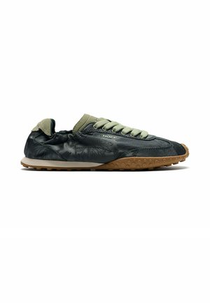 Zapatilla informal negra y verde oliva con cordones verde claro y suela de goma marrón con textura de panal.