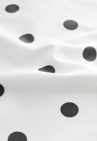 White fabric with distinct black polka dots in various sizes; smooth texture; subtle sheen enhances the pattern's visual contrast.