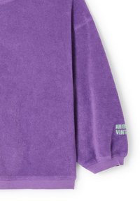 Manche longue en éponge violette d'un sweat-shirt avec poignet élastique et petit texte vert "AMER VINT" au niveau du poignet.
