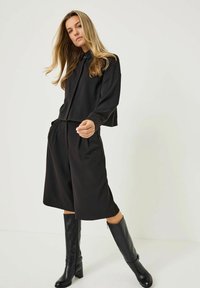 Černý outfit skládající se z krátkého topu s dlouhým rukávem a širokých šortek. Doplněn černými kozačkami do kolen, které mají jemnou texturu.