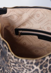 Handväska med leopardmönster och beige inredning, med en svart blixtlås ficka och hårdvara i guldton. Inuti finns ett mönster med "Café Noir"-logotyp.