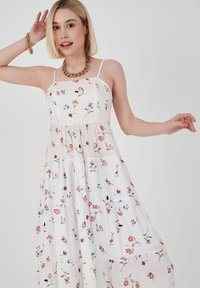 Maxikleid mit floralem Druck aus weißem Stoff, mit Spaghetti-Trägern, das einstufiges Design und zarte gestickte Blumen in verschiedenen Farben aufweist.