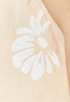 Triibuline kangas helesesami ja valgega, millel on tekstuuriga valgest lillede kujundus, millele on lisatud kaunistusi, rõhutades detaile ja kontrasti.