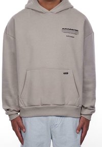 Sweat à capuche beige avec une poche frontale, des poignets et un ourlet côtelés. Présente un texte noir sur la poitrine indiquant "PROSIZE WORK HARD, STAY HUMBLE ELITE LEAGUE."